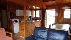 A cozy cabin interior with a wooden dining table, a blue leather sofa, a kitchenette with a microwave, and a small refrigerator. - Cozy chalet in a quiet, green area (Rendeux)