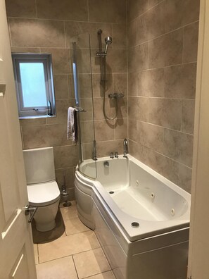 Een bad/douchecombinatie, een bubbelbad, een haardroger, handdoeken