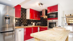 A modern kitchen with red cabinetry, stainless steel appliances, and a wooden table.
