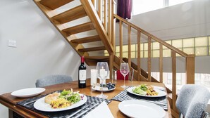 A dining area with a wooden table set for two, a bottle of wine, and a candle on the table.