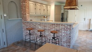 Una cocina con pared de ladrillo decorativa, gabinetes blancos, una isla central con taburetes y un ventanal grande.