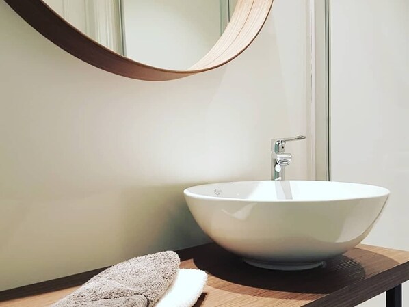 A bathroom with a white vessel sink, a wooden countertop, and a round mirror with a wooden frame.