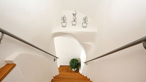 Una escalera de madera con paredes blancas y barandillas de metal, que conduce a un rellano con una planta en maceta.