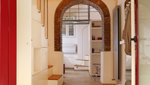 Un pasillo estrecho con un arco de ladrillo que conduce a una habitación con un radiador y una ventana.