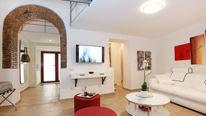 Una sala de estar moderna con un sofá blanco, otomanas rojas, una mesa de centro y un televisor montado en la pared.