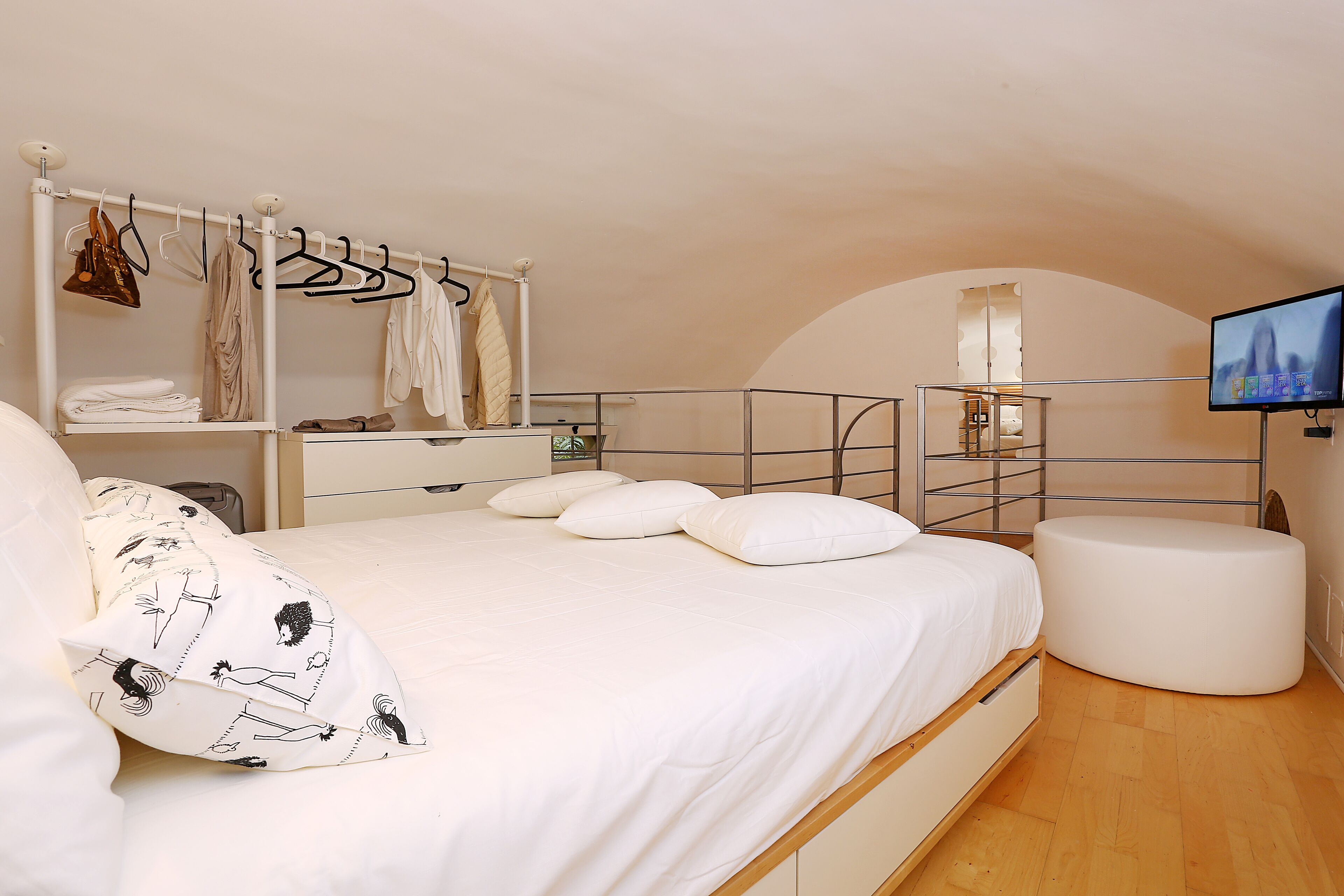 Une chambre avec un lit, un portant à vêtements, une télévision et un pouf rond.