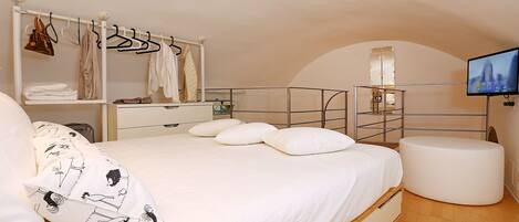 Une chambre avec un lit, un portant à vêtements, une télévision et un pouf rond.