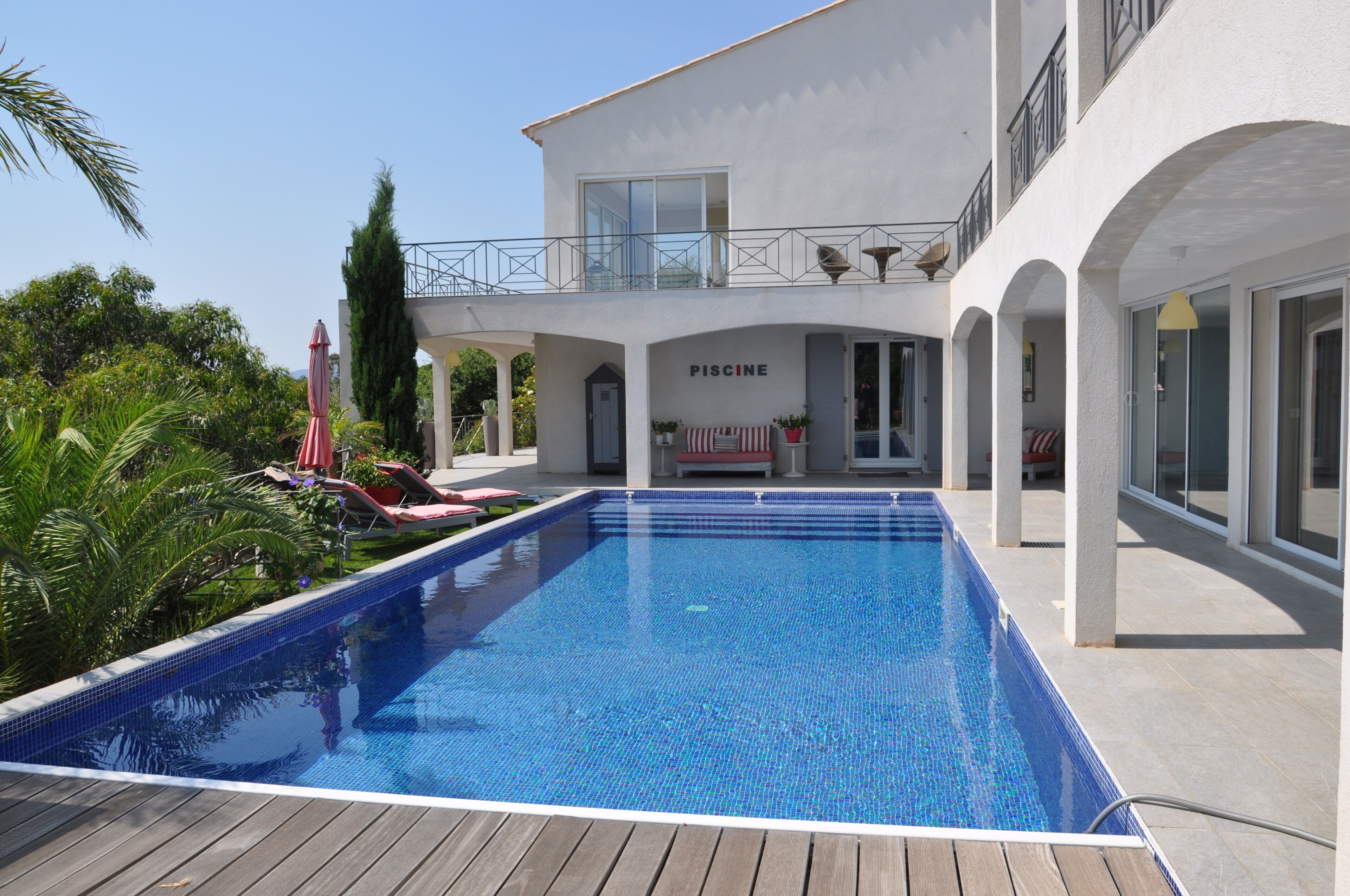 A swimming pool with a white building labeled "PISCINE" in the background, surrounded by greenery.