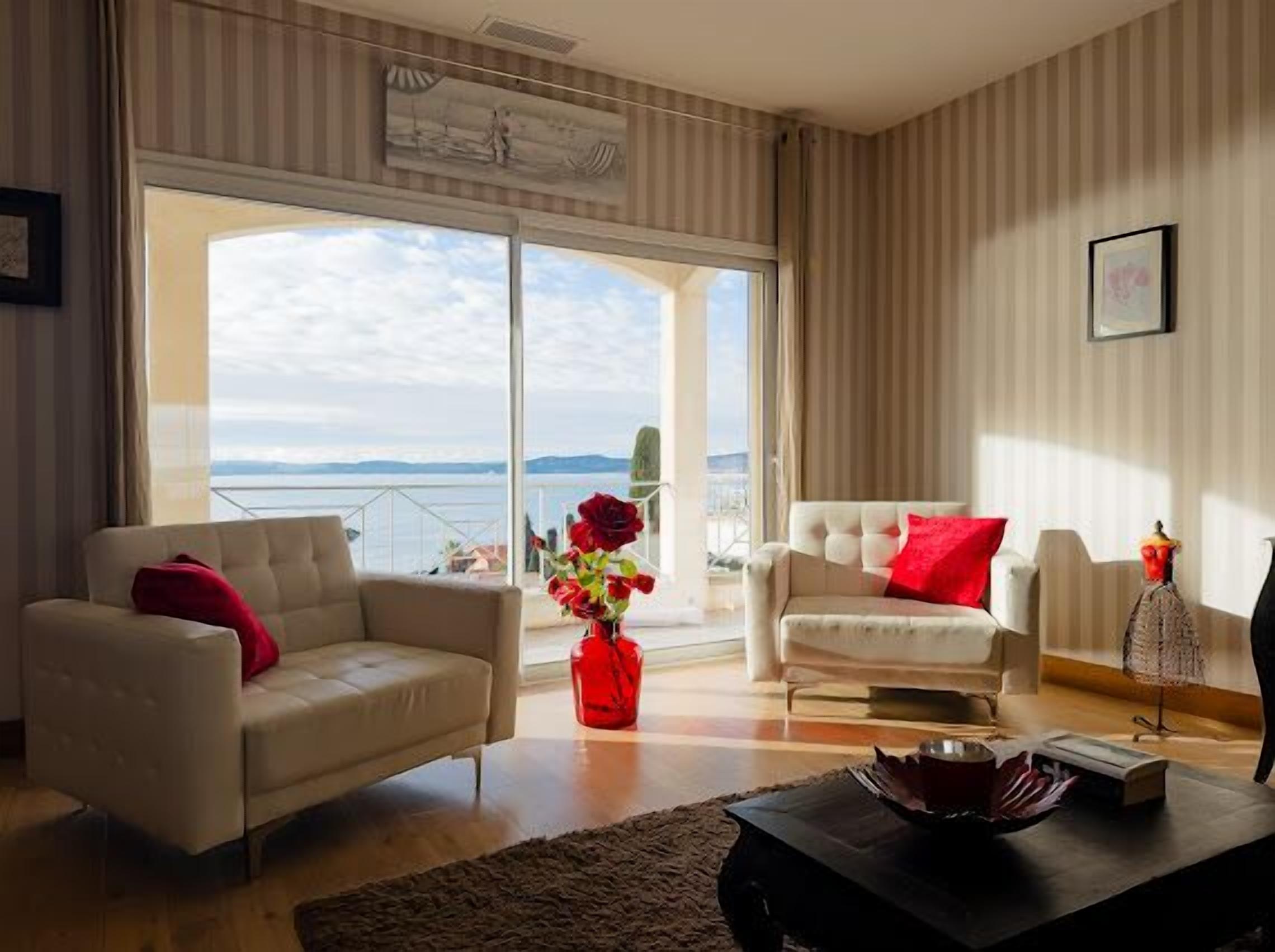 A spacious living room with two white sofas, a coffee table, and a view of the sea through large sliding doors.