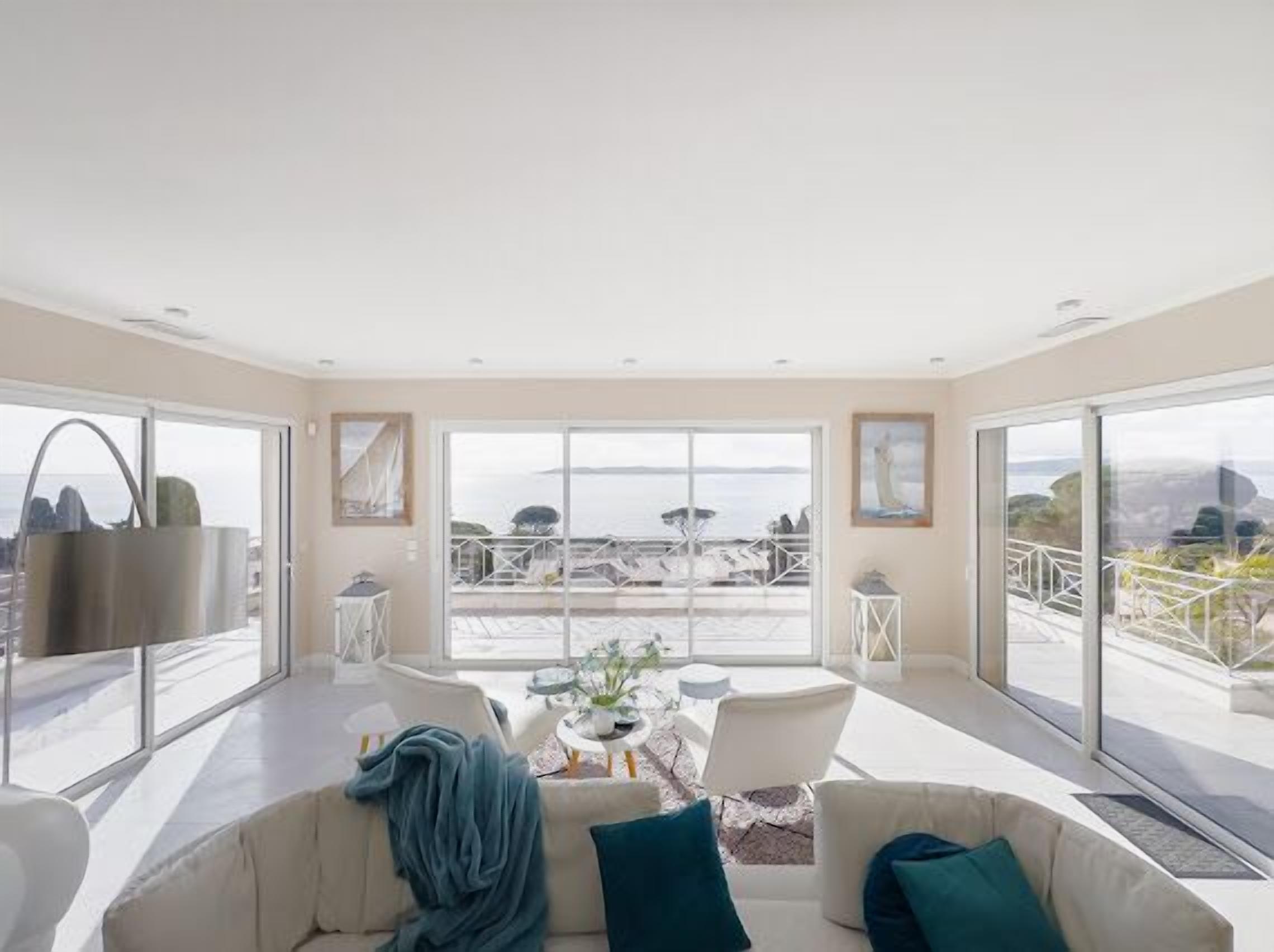 A spacious living room with a large window offering a view of the sea and distant land.