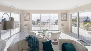 A spacious living room with a large window offering a view of the sea and distant land.