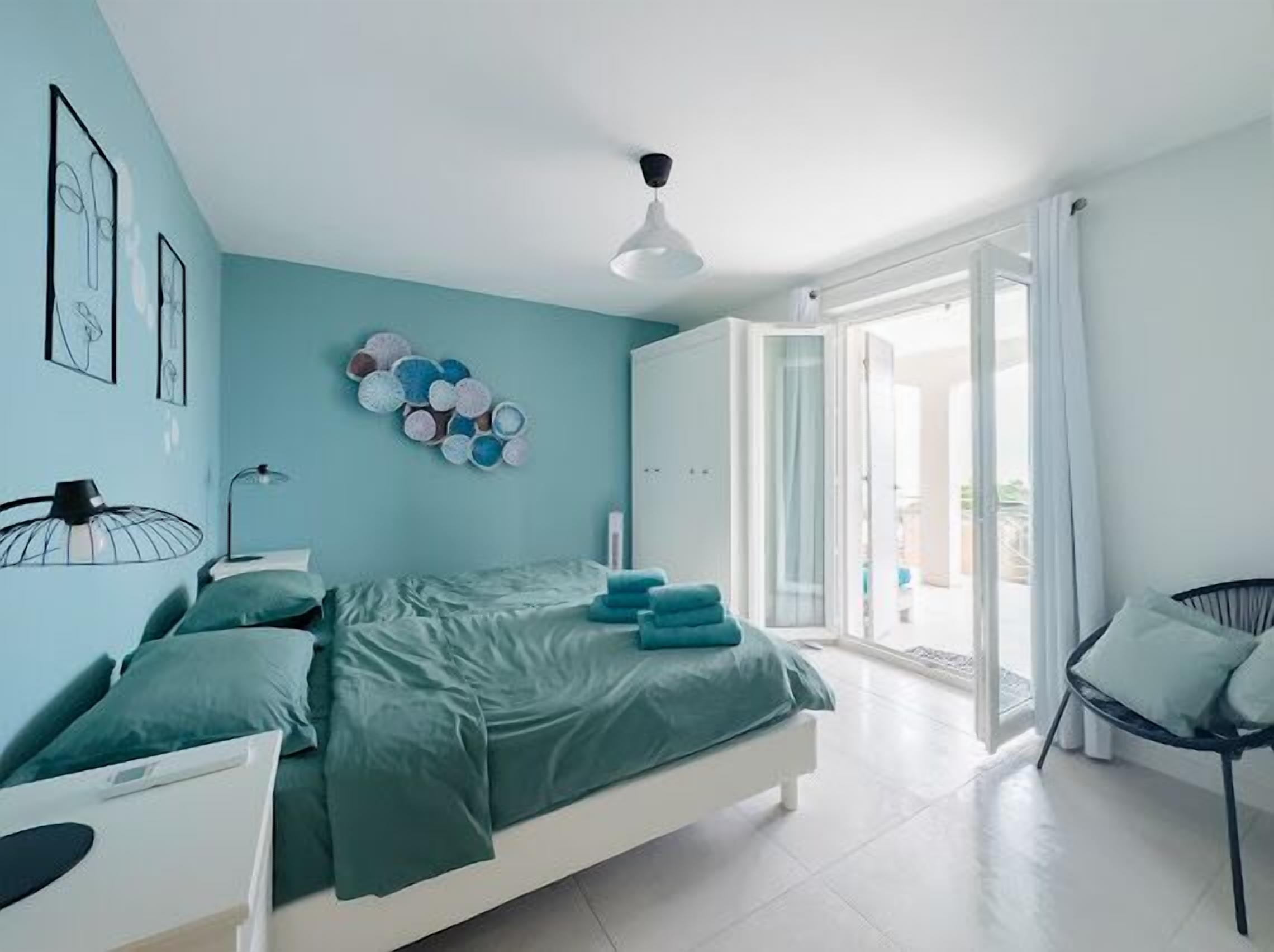 Um quarto moderno com cama, uma poltrona, uma obra de arte na parede e uma luminária de teto.