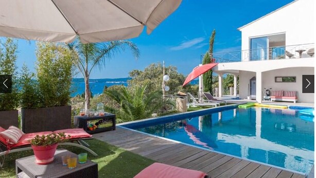 A modern pool area with a view of the ocean, a wooden deck, and outdoor seating.