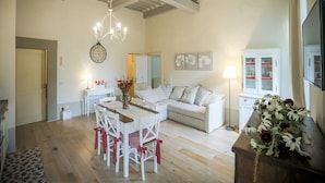 A spacious living area with a dining table, white chairs, a sofa, and a chandelier. - La Finestra sul Teatro  (Cortona)