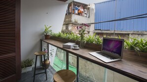 A balcony with a laptop, potted plants, and a view of a blue building.