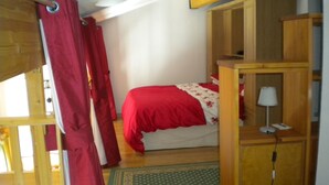 A bedroom with a bed, a wooden nightstand, a lamp, and a red curtain.