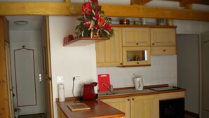 A kitchen with wooden cabinets, a coffee machine, a red cutting board, and a sink.