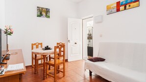 A living room with a white sofa, a dining table with chairs, a TV, and a painting on the wall. - Centro Vejer Apartment with Terraces and Beautiful Views (Vejer de la Frontera)