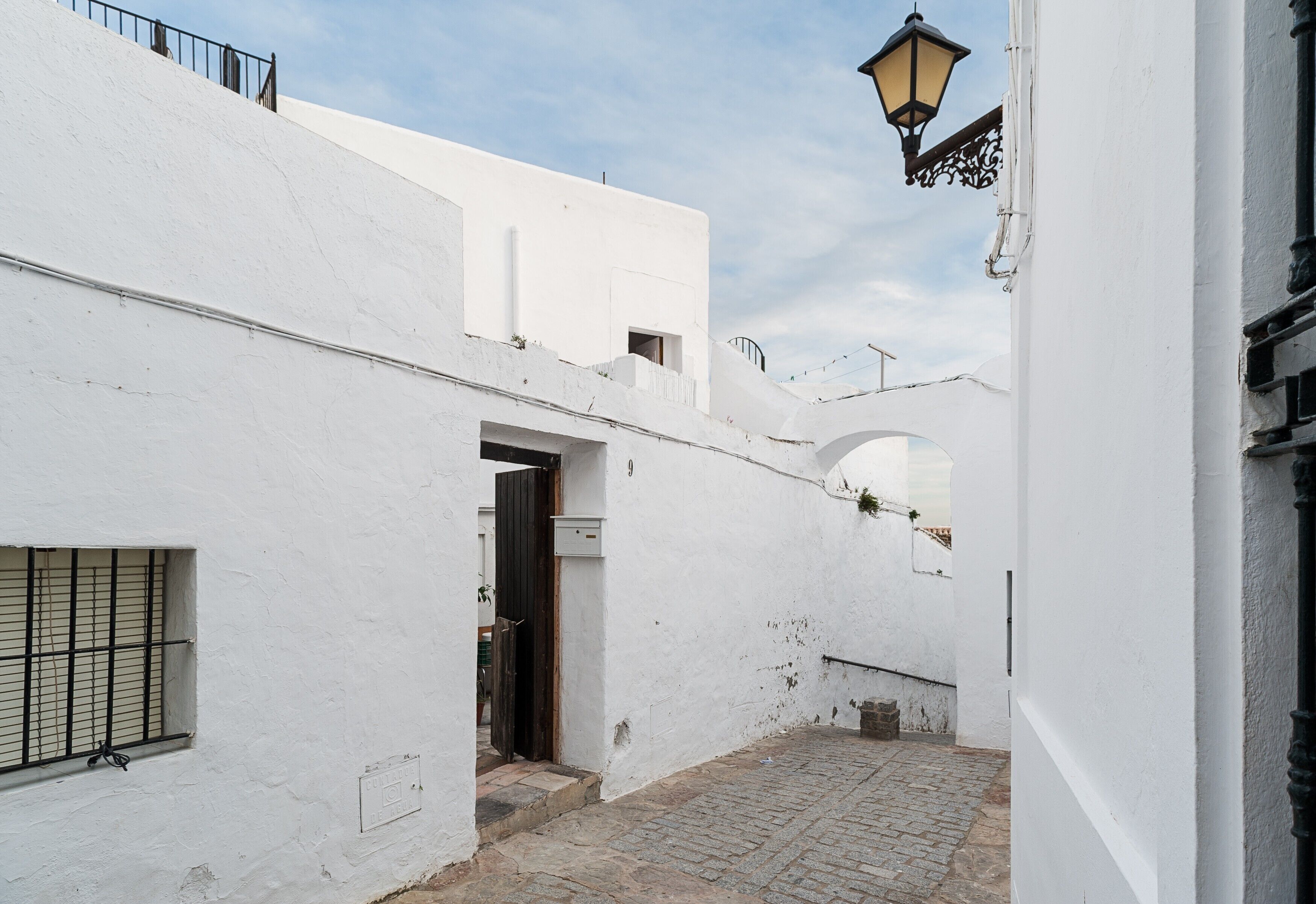 Un estrecho callejón con edificios blancos, una puerta de madera y un portón de metal.