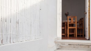 A white exterior wall with a window, a wooden door, and a staircase leading to an interior space with a table and chairs. - Centro Vejer Apartment with Terraces and Beautiful Views (Vejer de la Frontera)