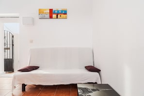 Ein weißes Sofa mit zwei Kissen, ein Fliesenboden, eine Wandklimaanlage und ein gerahmtes Kunstwerk über dem Sofa.