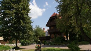 Ein traditionelles Holzgebäude mit rotem Dach, umgeben von üppigem Grün und einer Steinmauer.