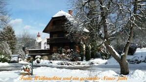 Ein traditionelles Holzhaus mit schneebedecktem Dach, umgeben von schneebedeckten Bäumen und einem klaren Himmel.