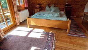 Ein gemütliches Schlafzimmer im Dachgeschoss mit Holzbalkendecke, einem Bett mit karierter Bettwäsche, einem Fenster mit Vorhängen und einer Heizung.