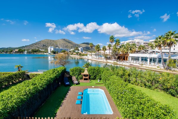 A pool area with a view of a body of water, a mountain, and a resort building.