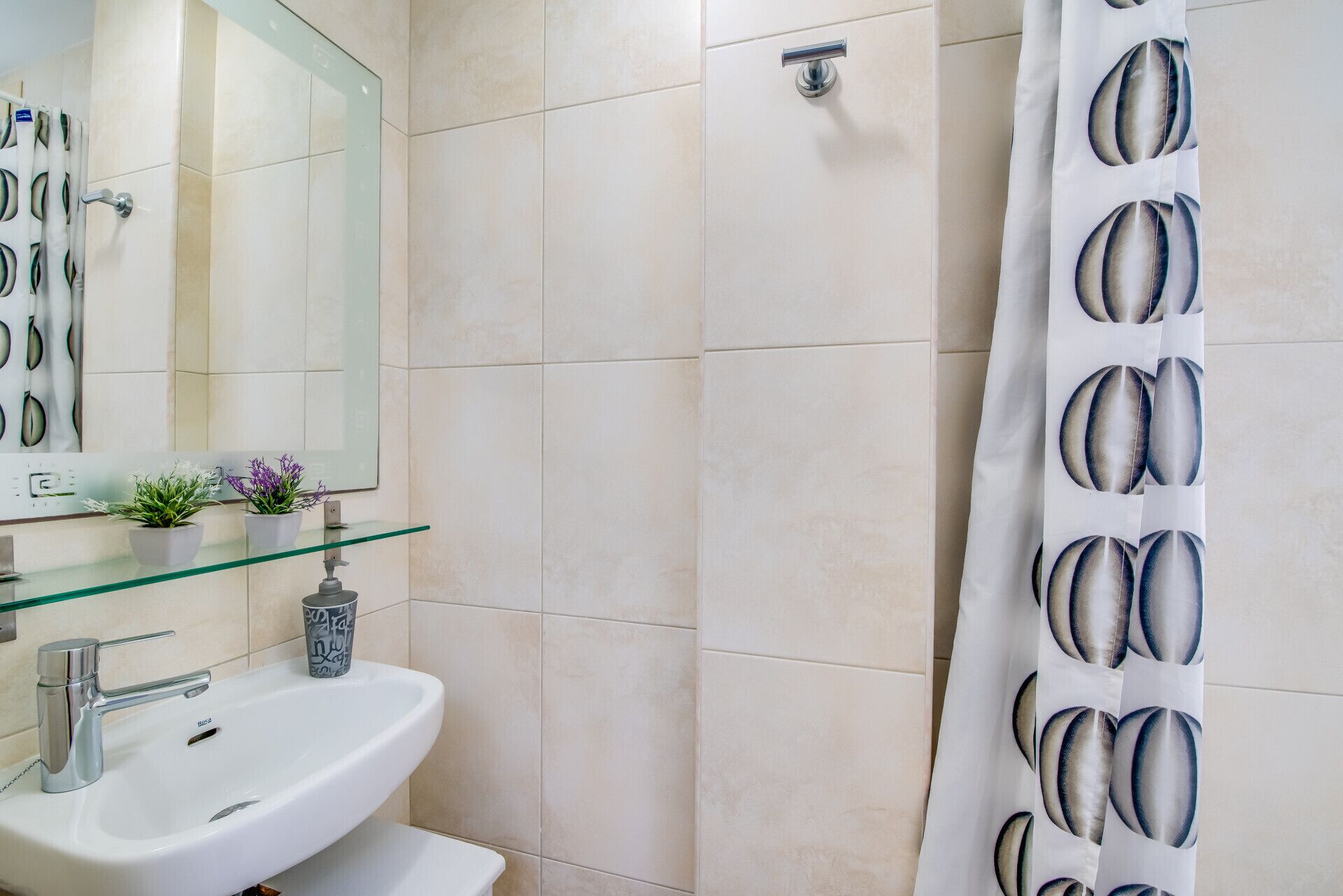 A modern bathroom with a glass shelf, a white sink, a mirror, and a shower curtain with a pattern.