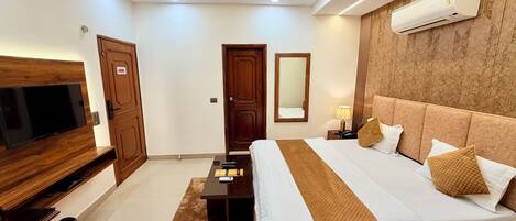 A hotel room with a bed, TV, ceiling fan, air conditioning unit, and a mirror.