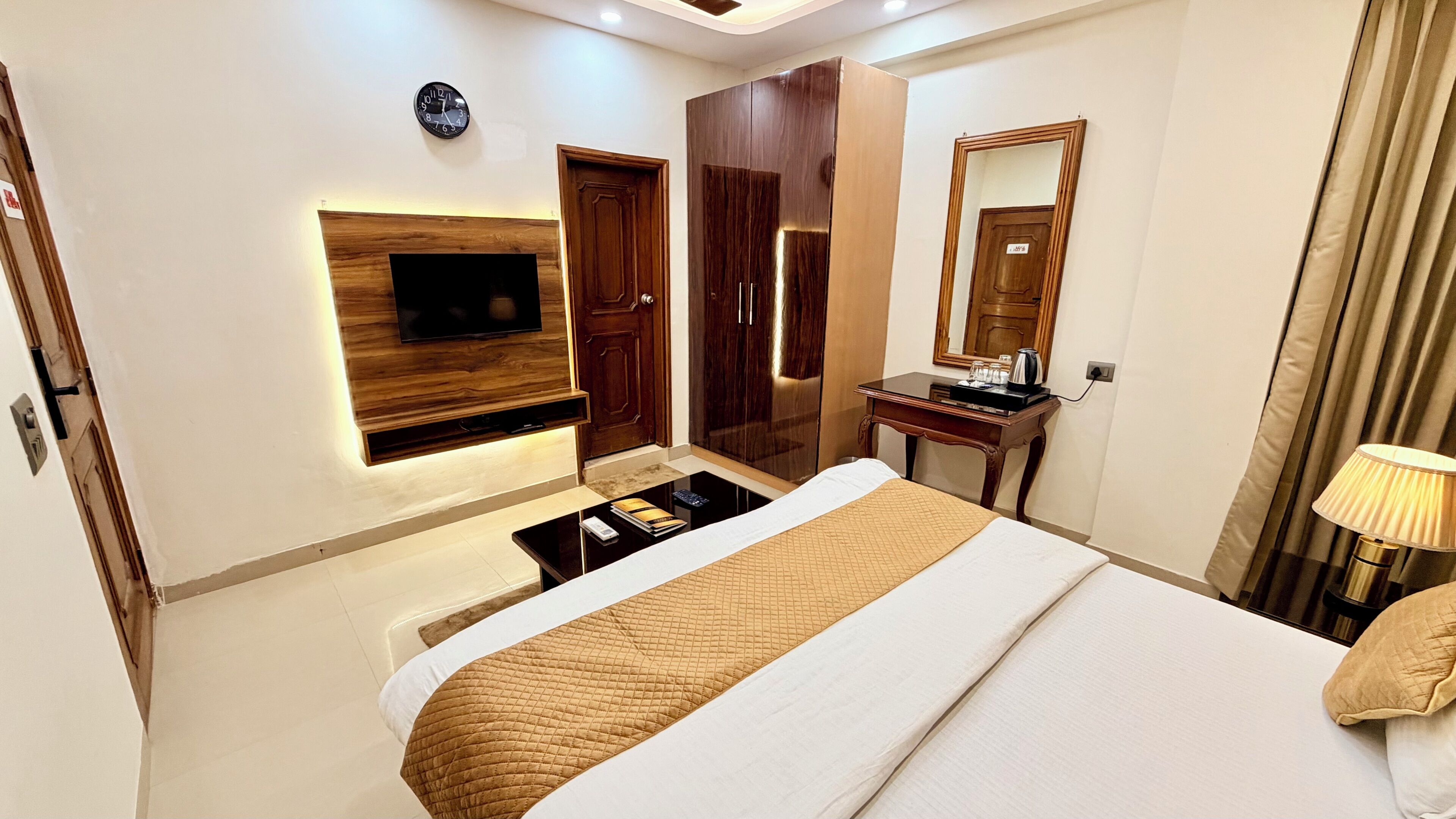 Une chambre d’hôtel comprenant un lit, un téléviseur fixé au mur, un bureau avec un miroir et une armoire.
