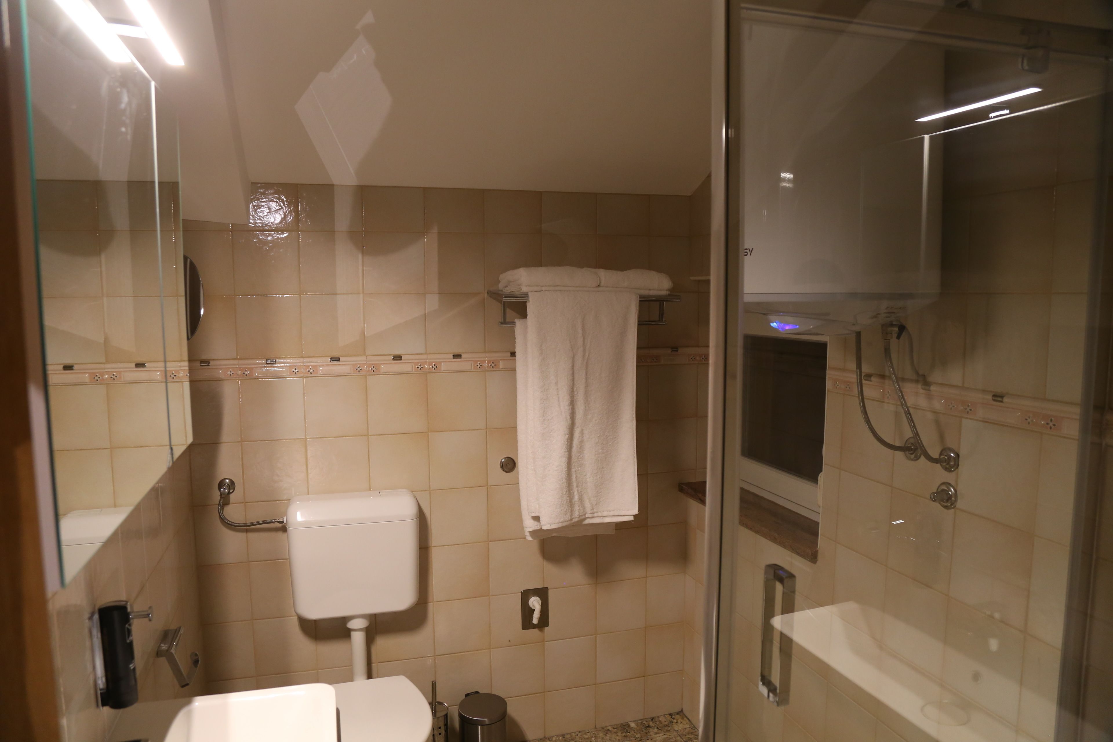 Un baño con inodoro, ducha con mampara de vidrio y perchero para toallas.