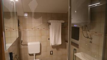 Un baño con inodoro, ducha con mampara de vidrio y perchero para toallas.