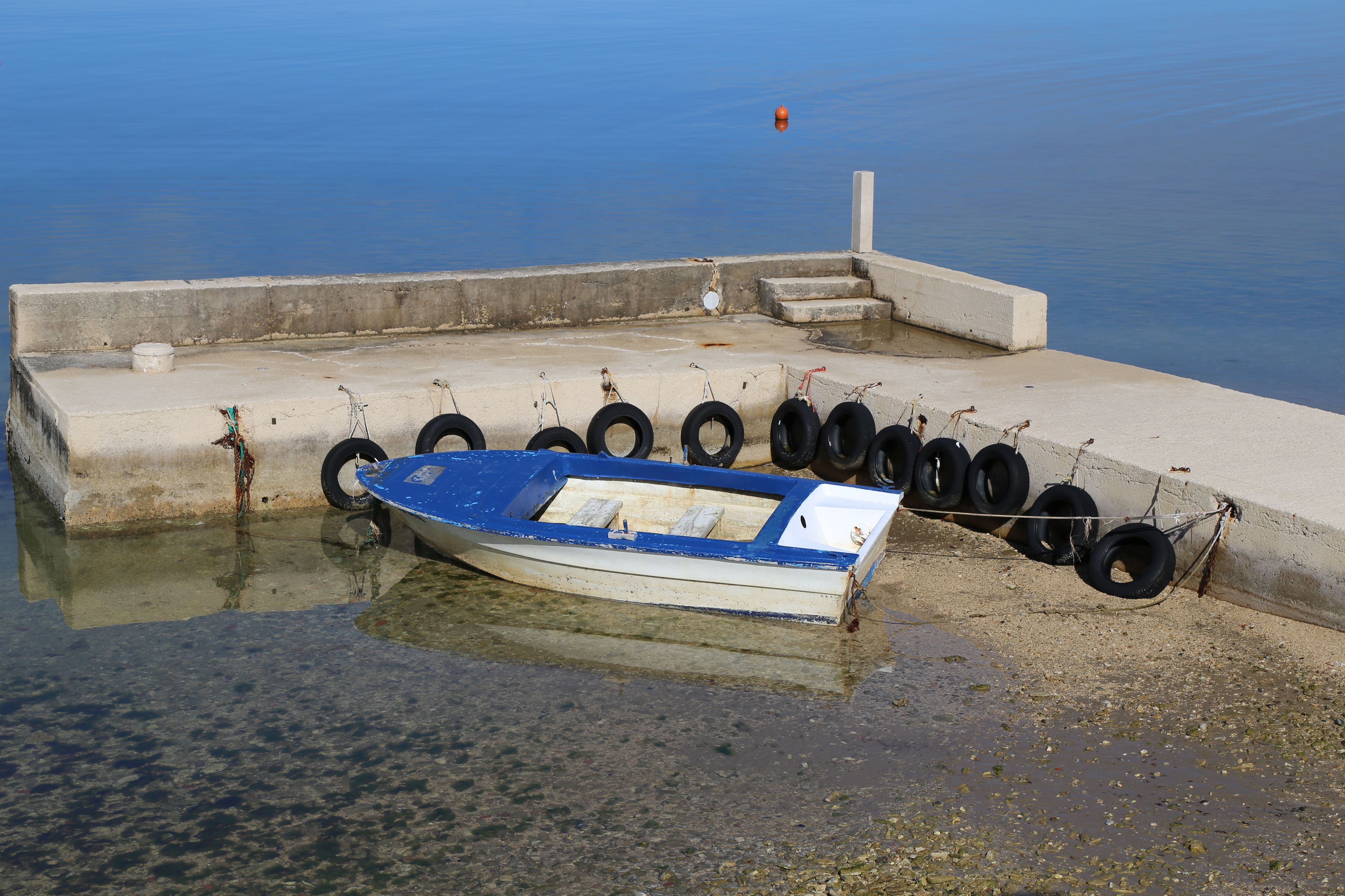 Una pequeña embarcación azul atada a un muelle de hormigón con neumáticos.