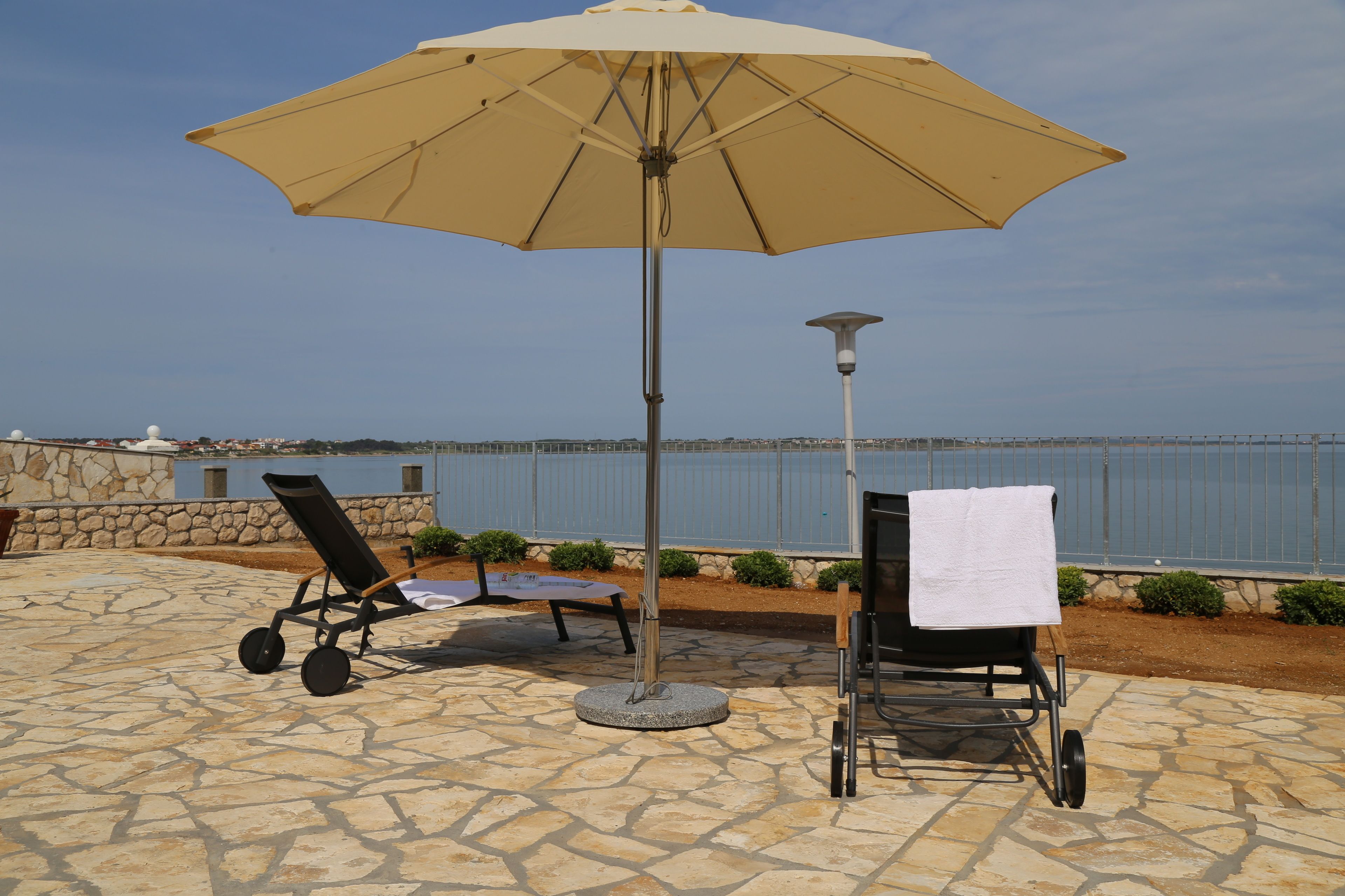 An outdoor seating area with a stone patio, a large umbrella, and a view of the sea.