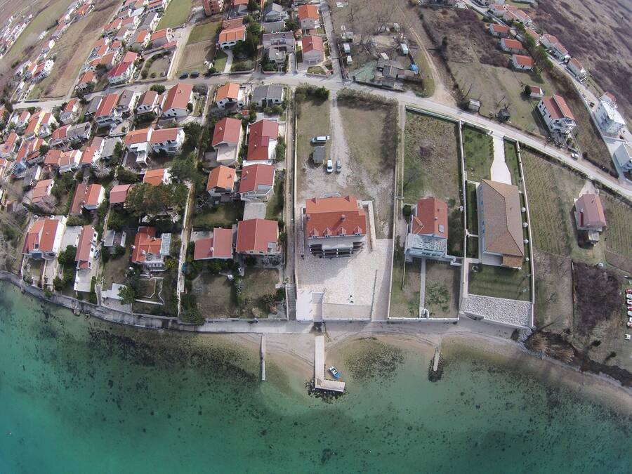 An aerial view of a coastal residential area with houses, a marina, and a road.