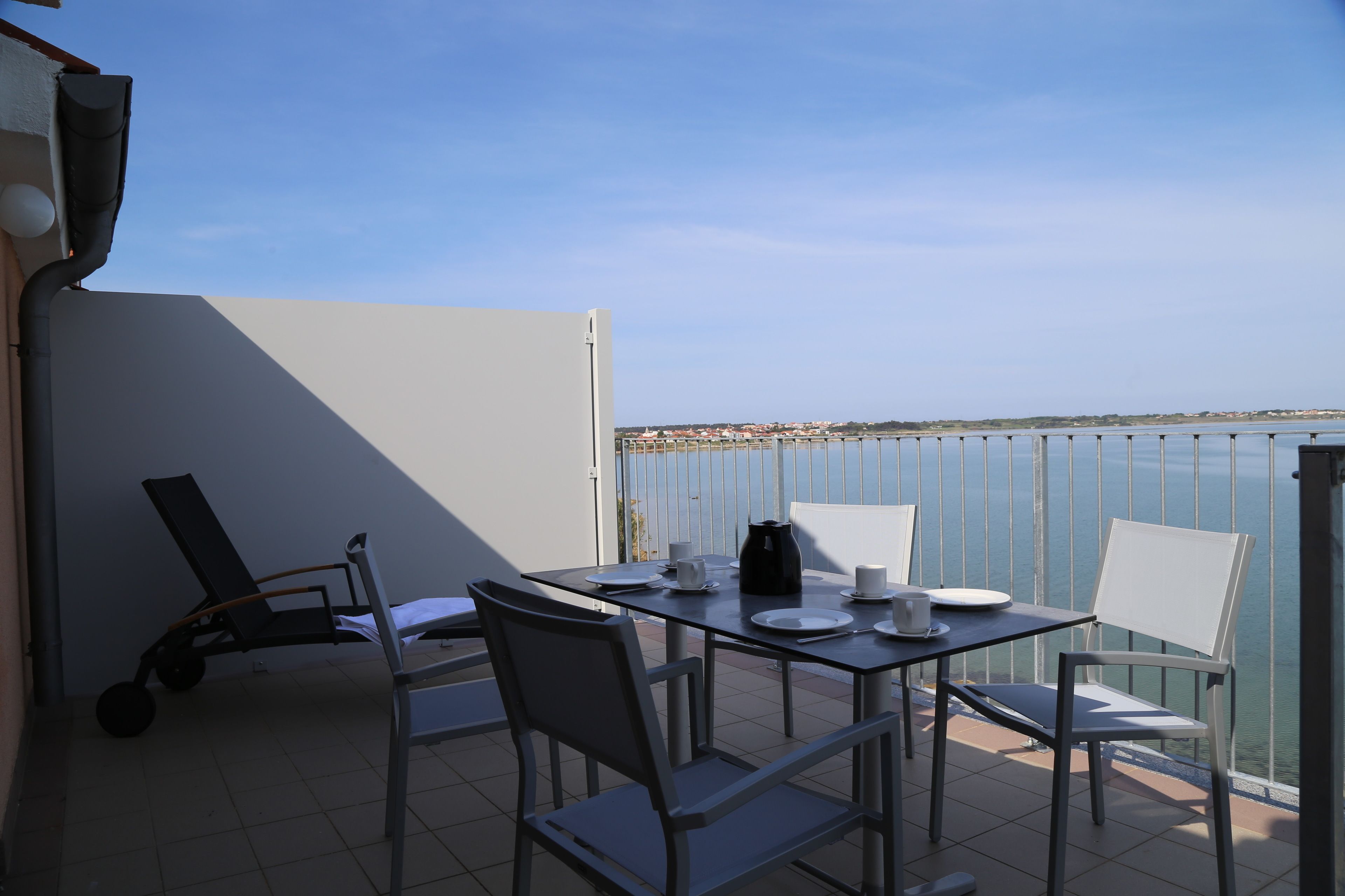 A balcony with a table set for two, chairs, and a view of the sea.