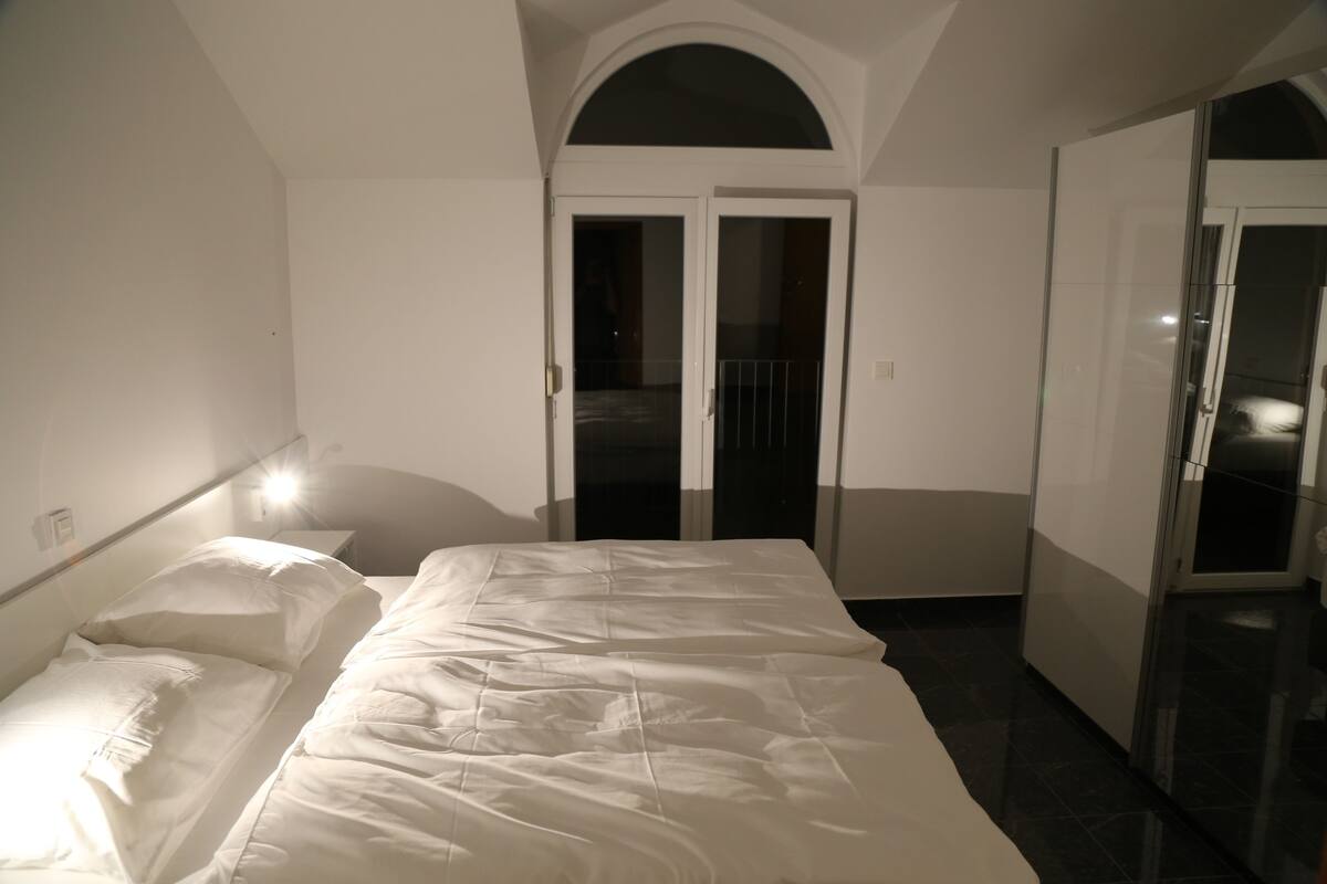 A bedroom with a bed, a wardrobe, and a door leading to another room.
