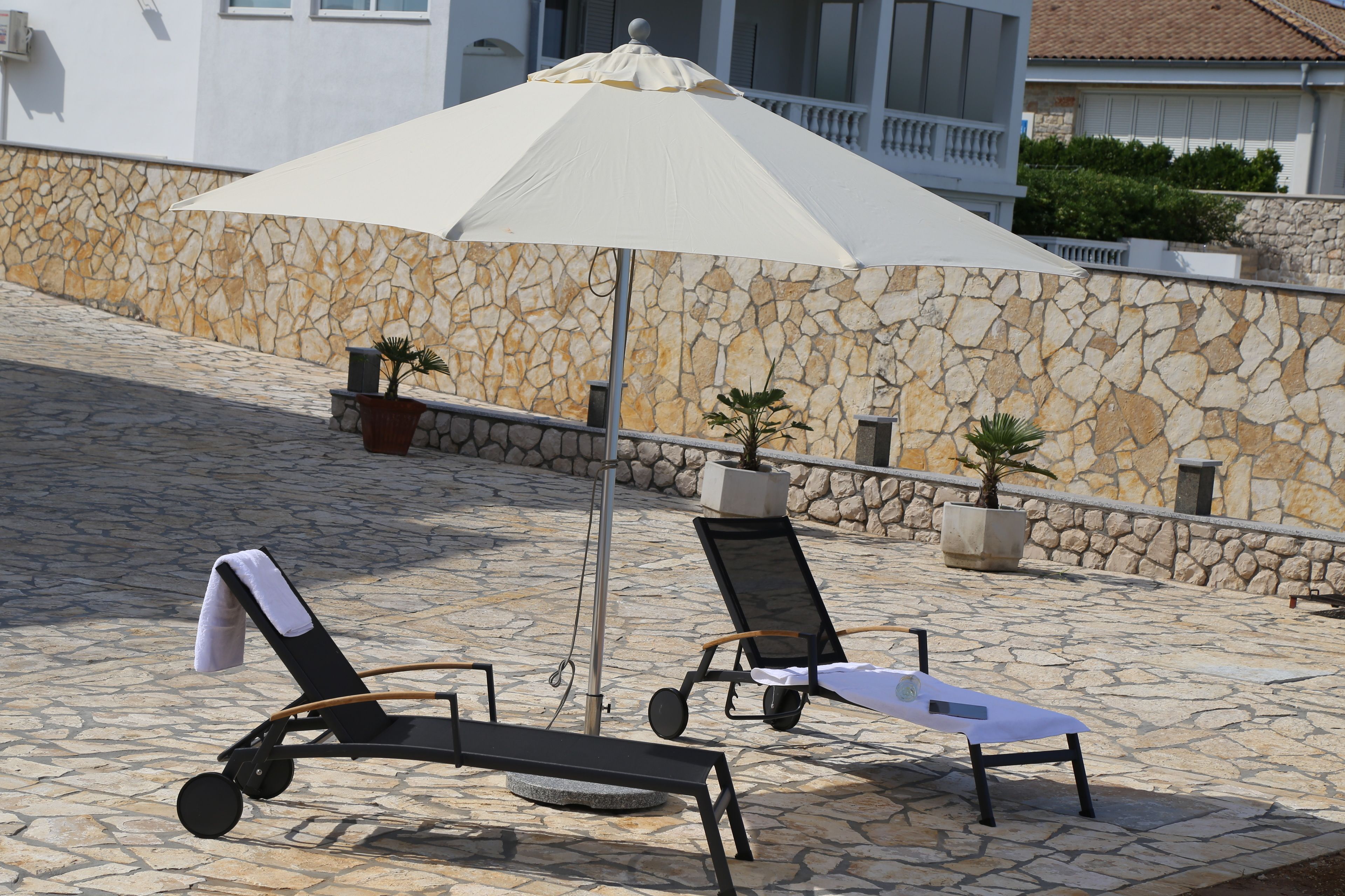 A stone-paved outdoor area with two lounge chairs and a large umbrella.