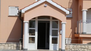 A building entrance with a stone base, a white door, and a small balcony with a railing. - mk | apartments nin (Vrsi)