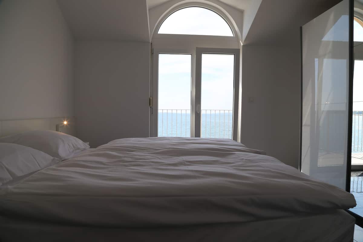 A bedroom with a large bed, a skylight, and a view of the sea.