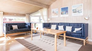 Ein gemütliches Zimmer mit Holzbalkendecke, einem blau gestreiften Sofagarnitur, einem Holztisch und einem großen Fenster mit Vorhängen.