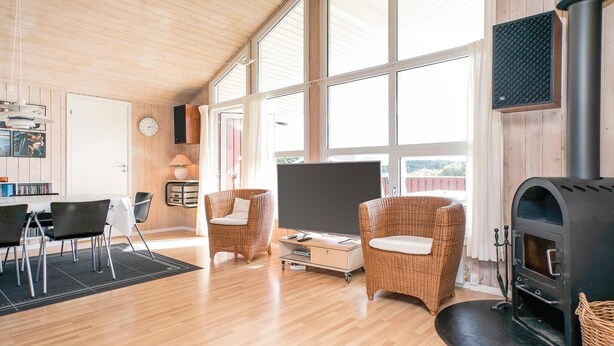 Ein gemütliches Wohnzimmer mit Kamin, Korbmöbeln, Fernseher und einem großen Fenster.