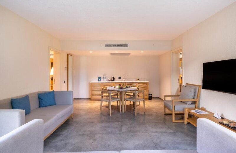 A modern living room with a sofa, dining table, chairs, and a TV mounted on the wall.