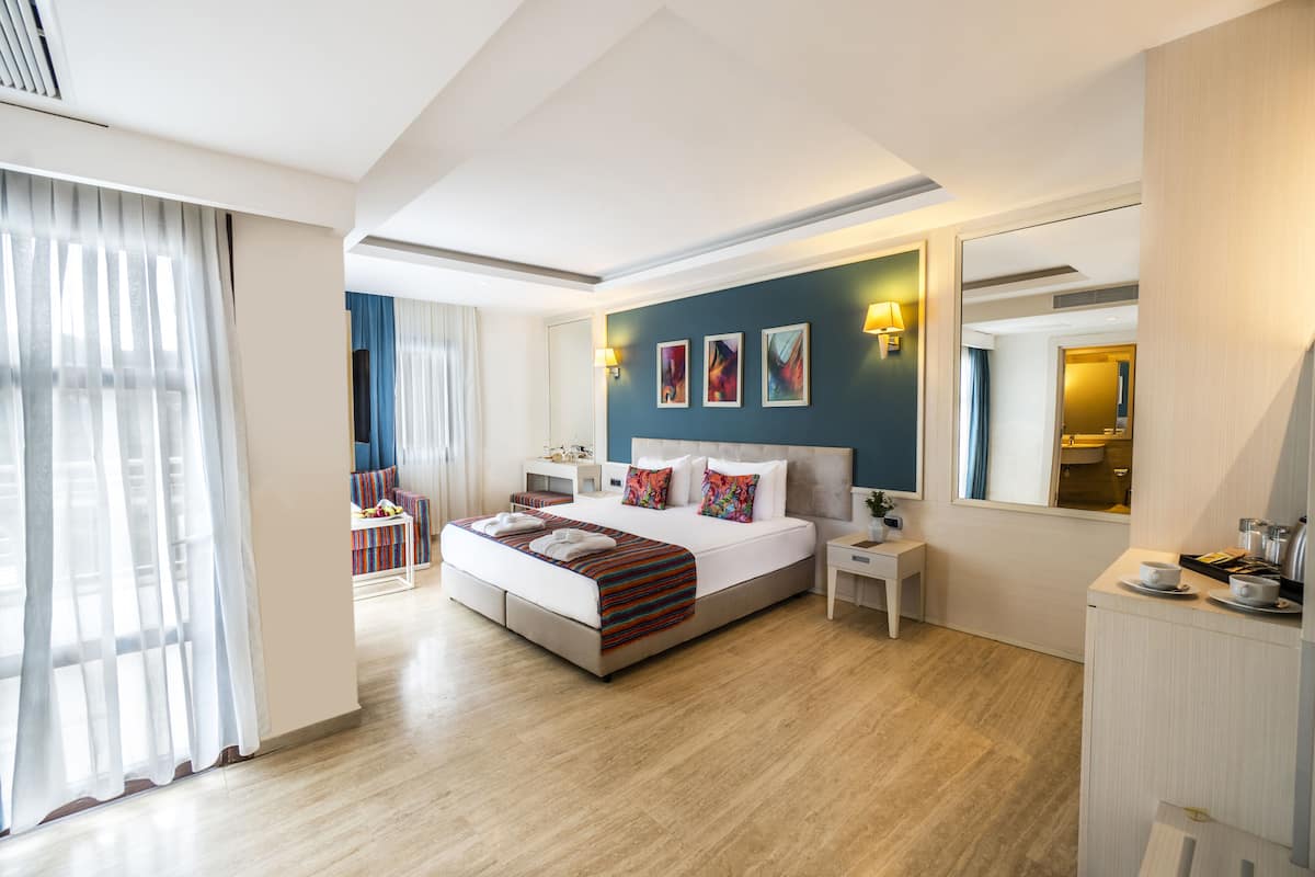 A modern hotel room with a large bed, bedside tables, a desk, and a mirror.