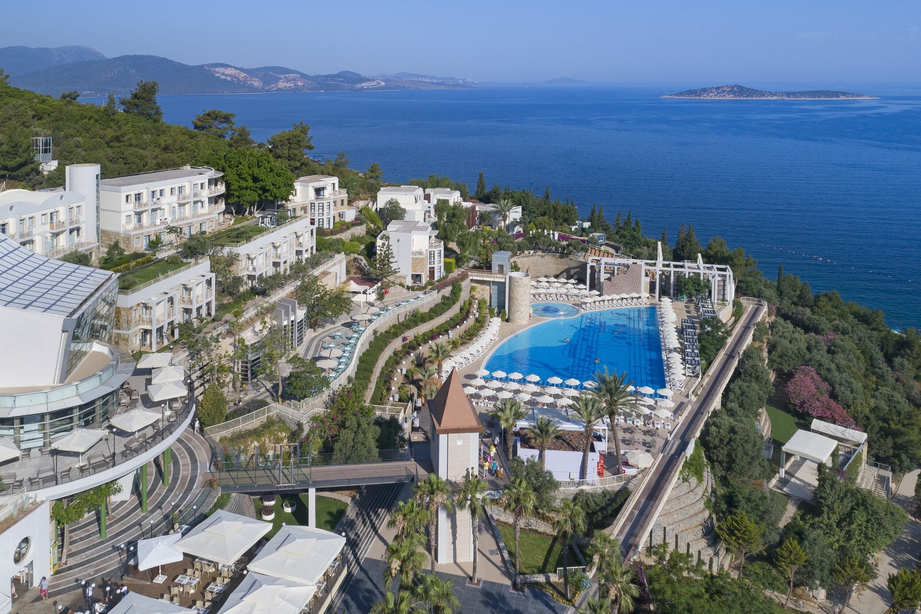 A resort with a large pool, multiple buildings, and a view of the sea.