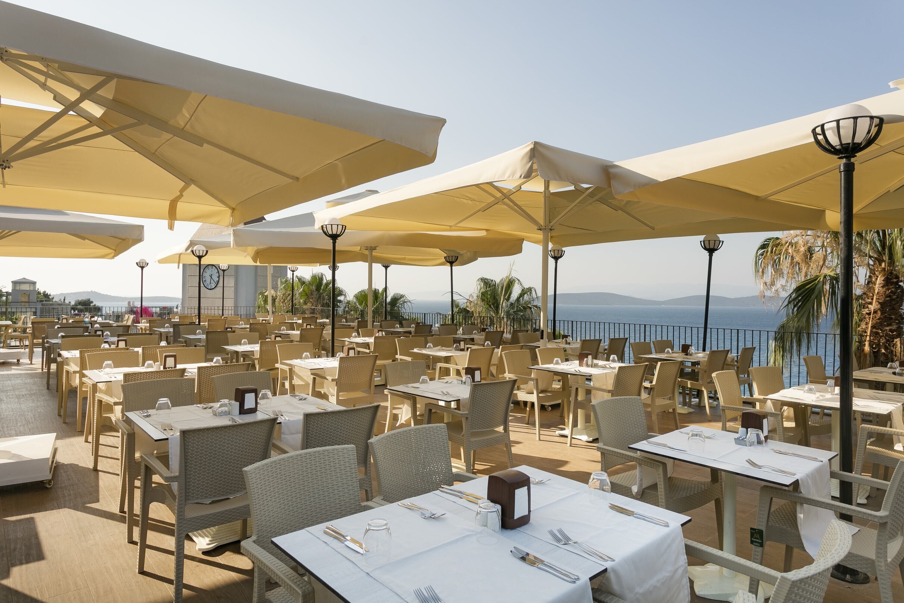 An outdoor dining area with tables and chairs, umbrellas, and a view of the sea.