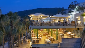 A multi-level outdoor dining area with tables and umbrellas, surrounded by palm trees and a mountainous backdrop. - Duja Bodrum - All Inclusive (Bodrum)