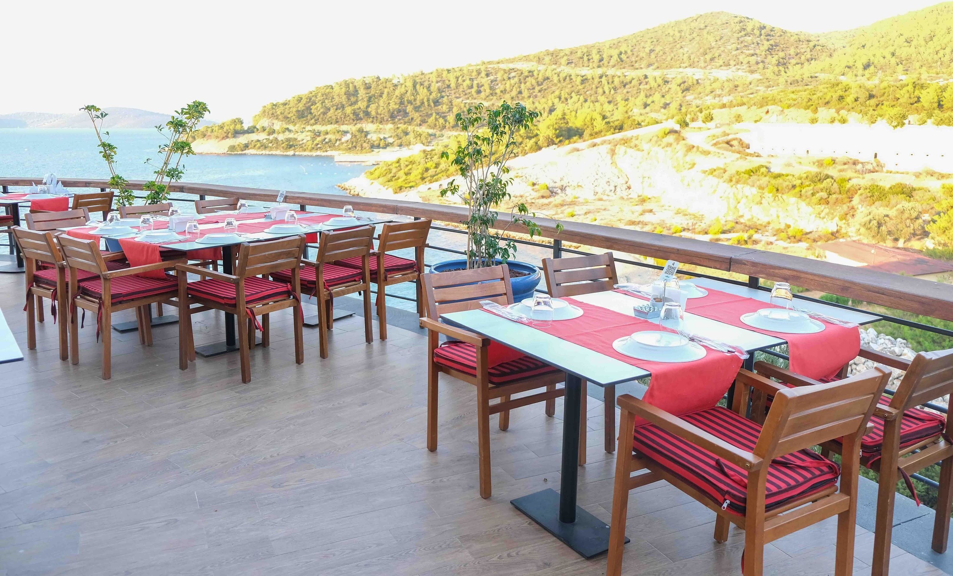 An outdoor dining area with tables and chairs, overlooking a coastal landscape.